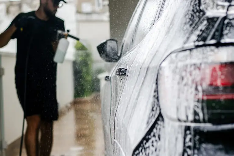 profissional uniformizado bizlimp aplicando shampoo com snowfoan durante lavagem na garagem